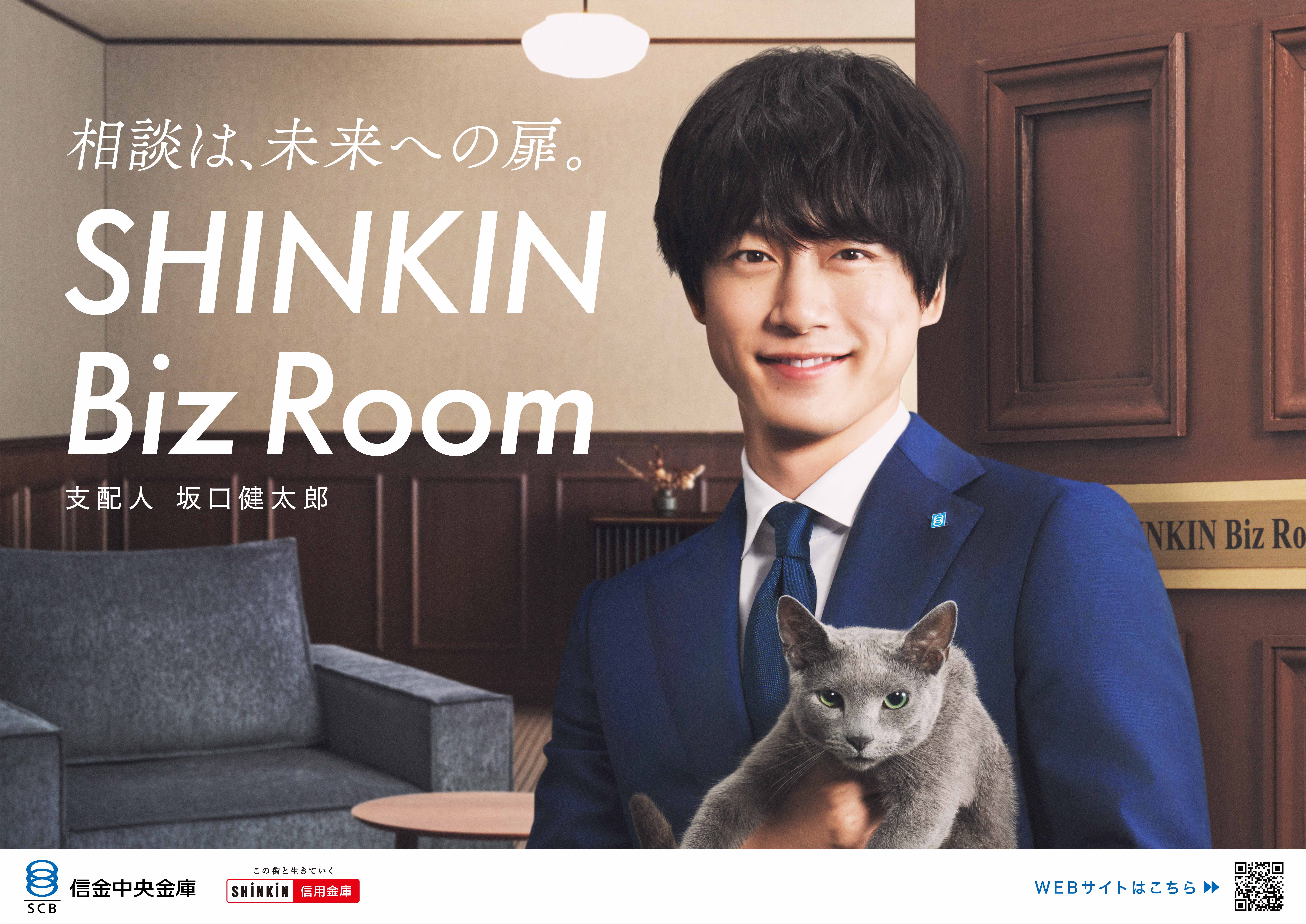 相談は、未来への扉。SHINKIN Biz Room 支配人 坂口健太郎 スーツ姿の坂口健太郎が笑顔で猫を抱き、木製の扉の前に立っている。背景は応接室のような落ち着いた室内。