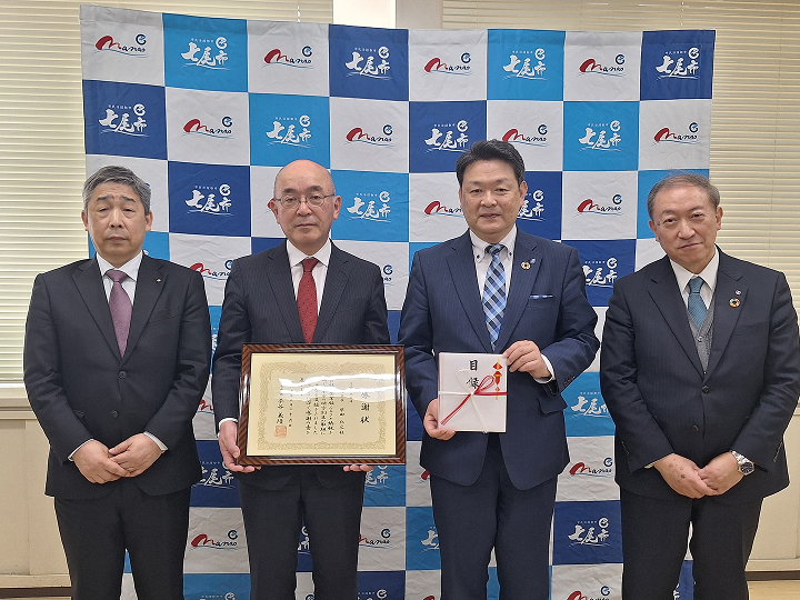 スーツ姿の関係者が感謝状・目録を手にして撮影した贈呈式の集合写真。七飯町の会場。